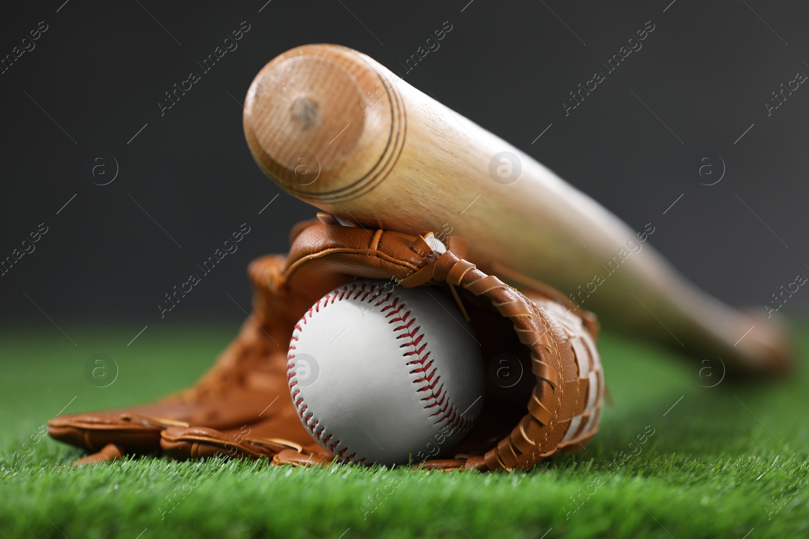 Photo of Baseball bat, leather glove and ball on green grass against dark background, closeup