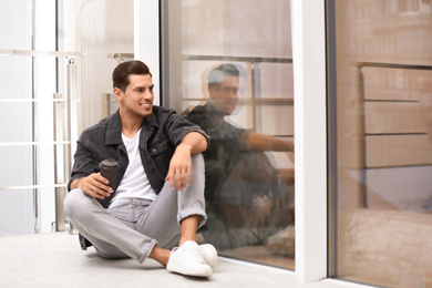 Photo of Handsome man with paper cup of coffee near window at home