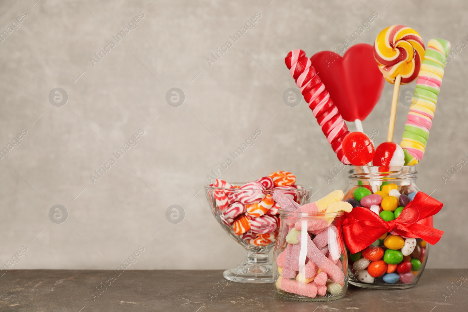 Photo of Jars with different delicious candies on grey table, space for text