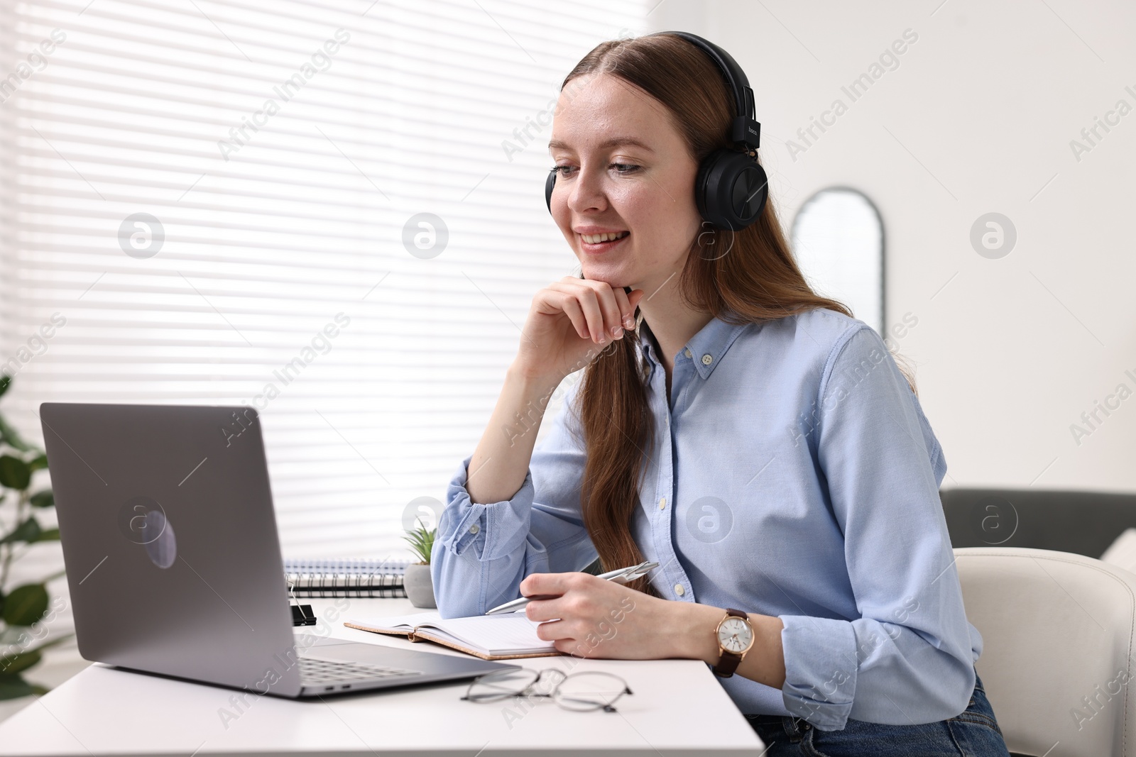 Photo of E-learning. Young woman using laptop during online lesson at white table indoors