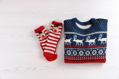 Photo of Christmas sweater and socks with pattern on wooden background, top view