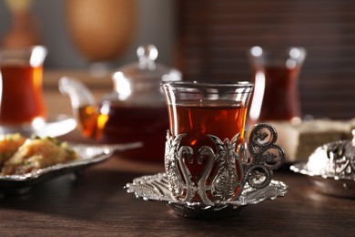 Photo of Glass of traditional Turkish tea in vintage holder on wooden table