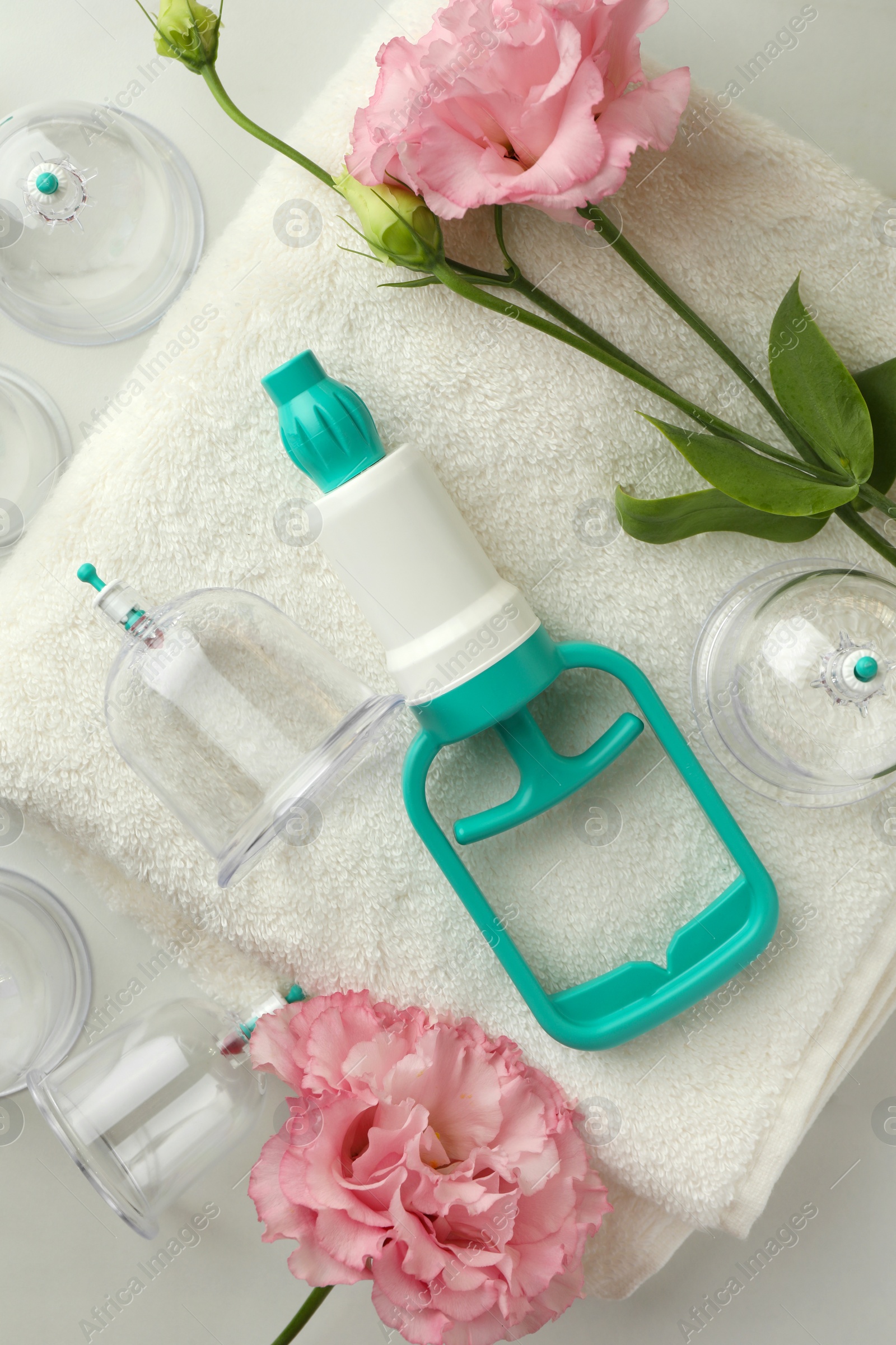 Photo of Plastic cups, hand pump, flowers and towel on white table, flat lay. Cupping therapy