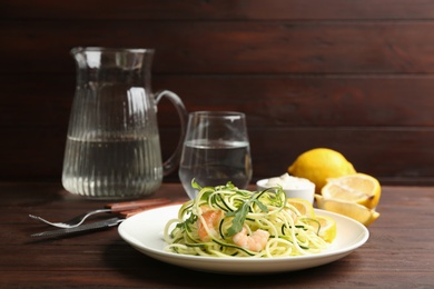 Photo of Delicious zucchini pasta with arugula and shrimps served on wooden table. Space for text