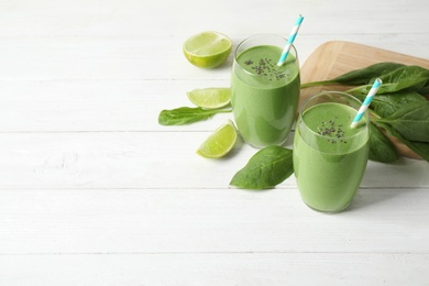 Photo of Glasses of healthy green smoothie with fresh spinach on white wooden table. Space for text