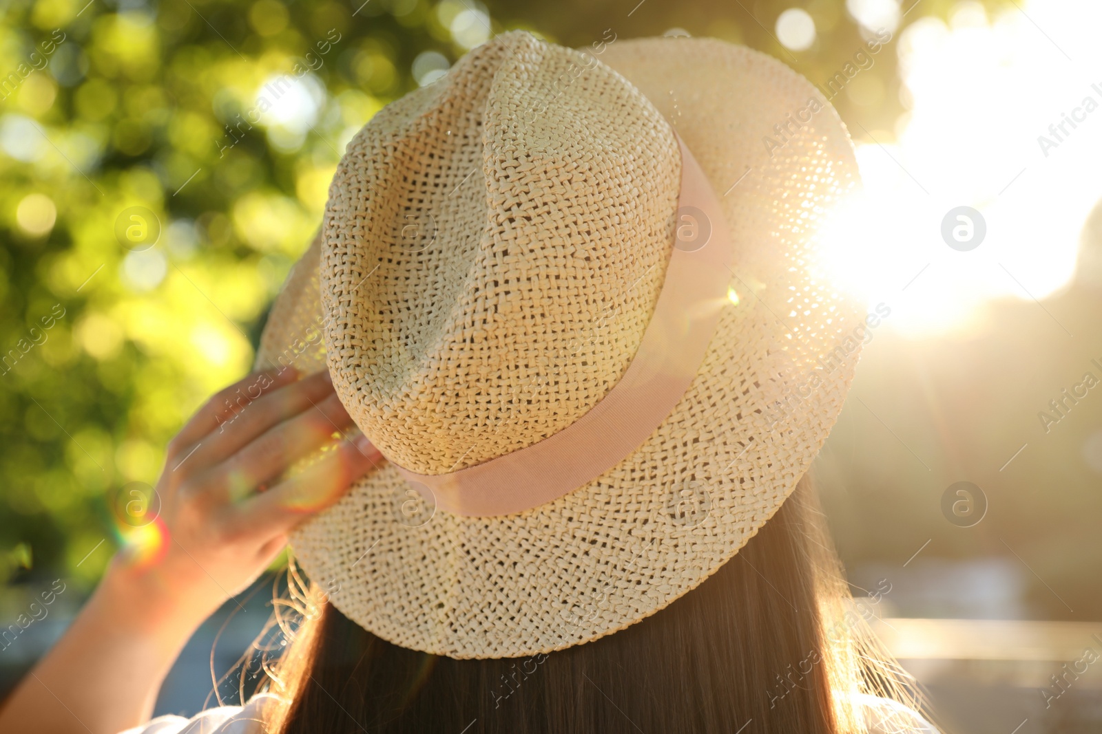 Photo of Young woman in hat outdoors on sunny day, back view