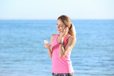 Young woman choosing music for fitness exercises on beach in morning