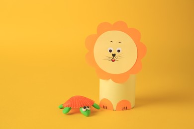 Photo of Toy lion made from toilet paper hub and plasticine turtle on yellow background. Children's handmade ideas