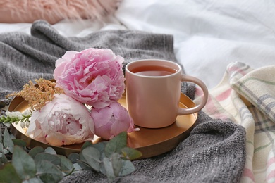 Photo of Tray with cup of tea and beautiful bouquet on bed