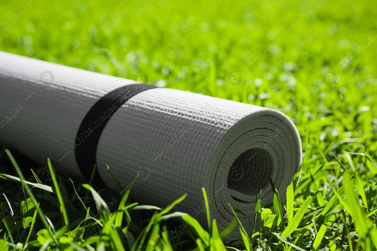 Photo of Rolled karemat or fitness mat on green grass outdoors, closeup