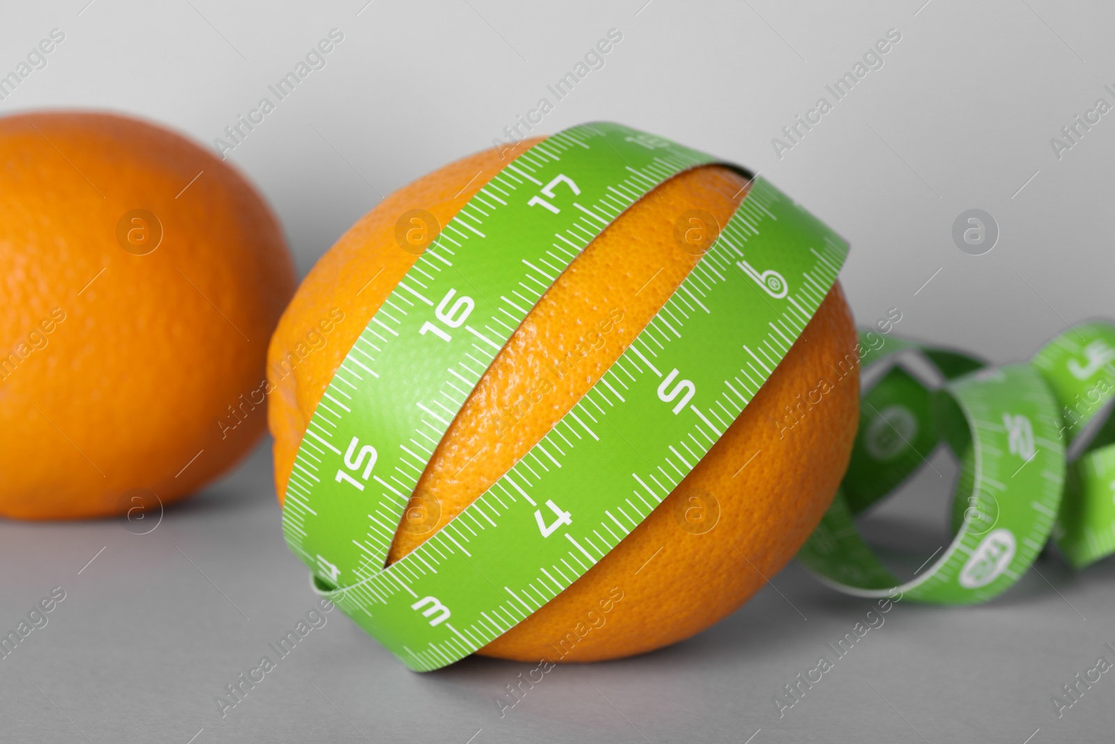 Photo of Cellulite problem. Oranges and measuring tape on light grey background, closeup