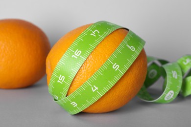 Photo of Cellulite problem. Oranges and measuring tape on light grey background, closeup