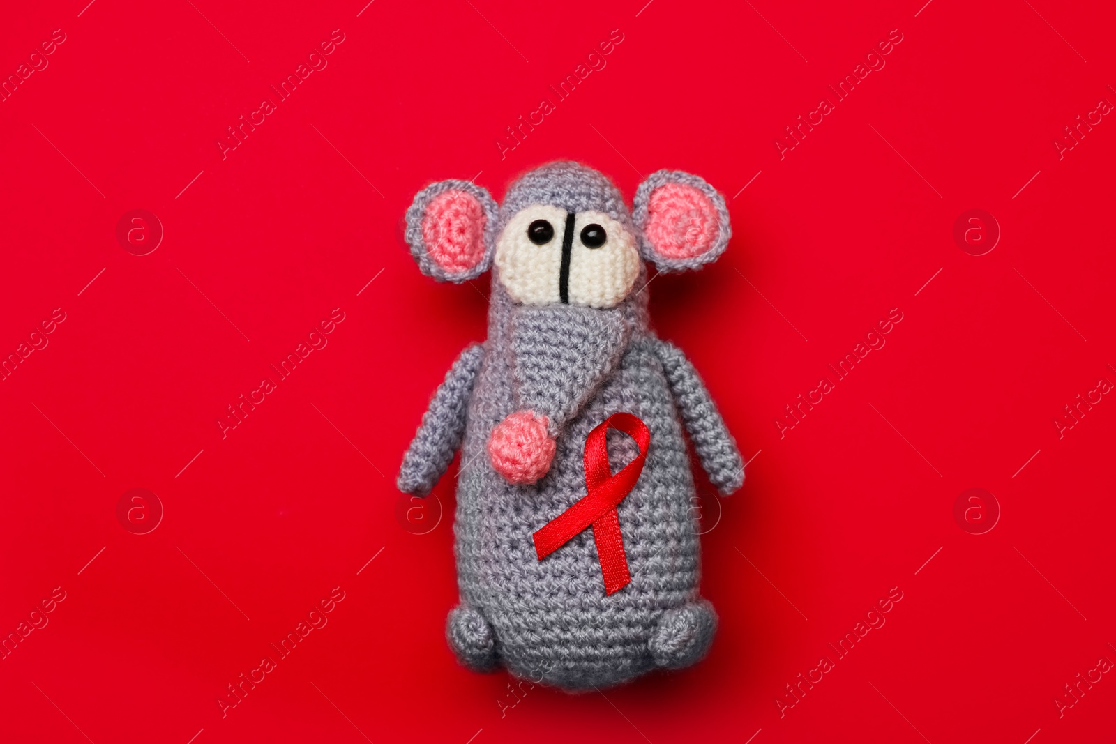 Photo of Cute knitted toy mouse with ribbon on red background, top view. AIDS disease awareness