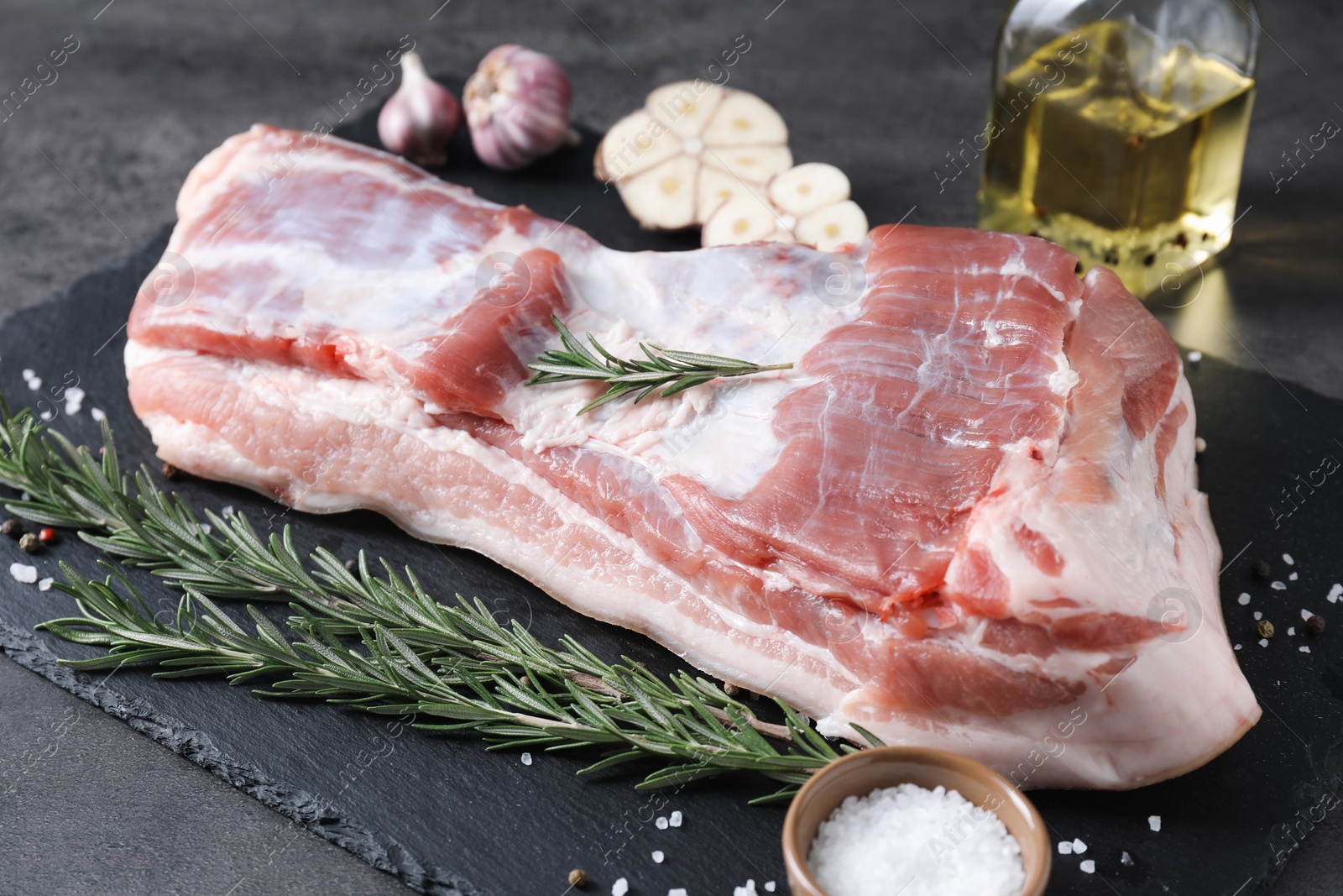 Photo of Piece of raw pork belly, rosemary, garlic and salt on grey table