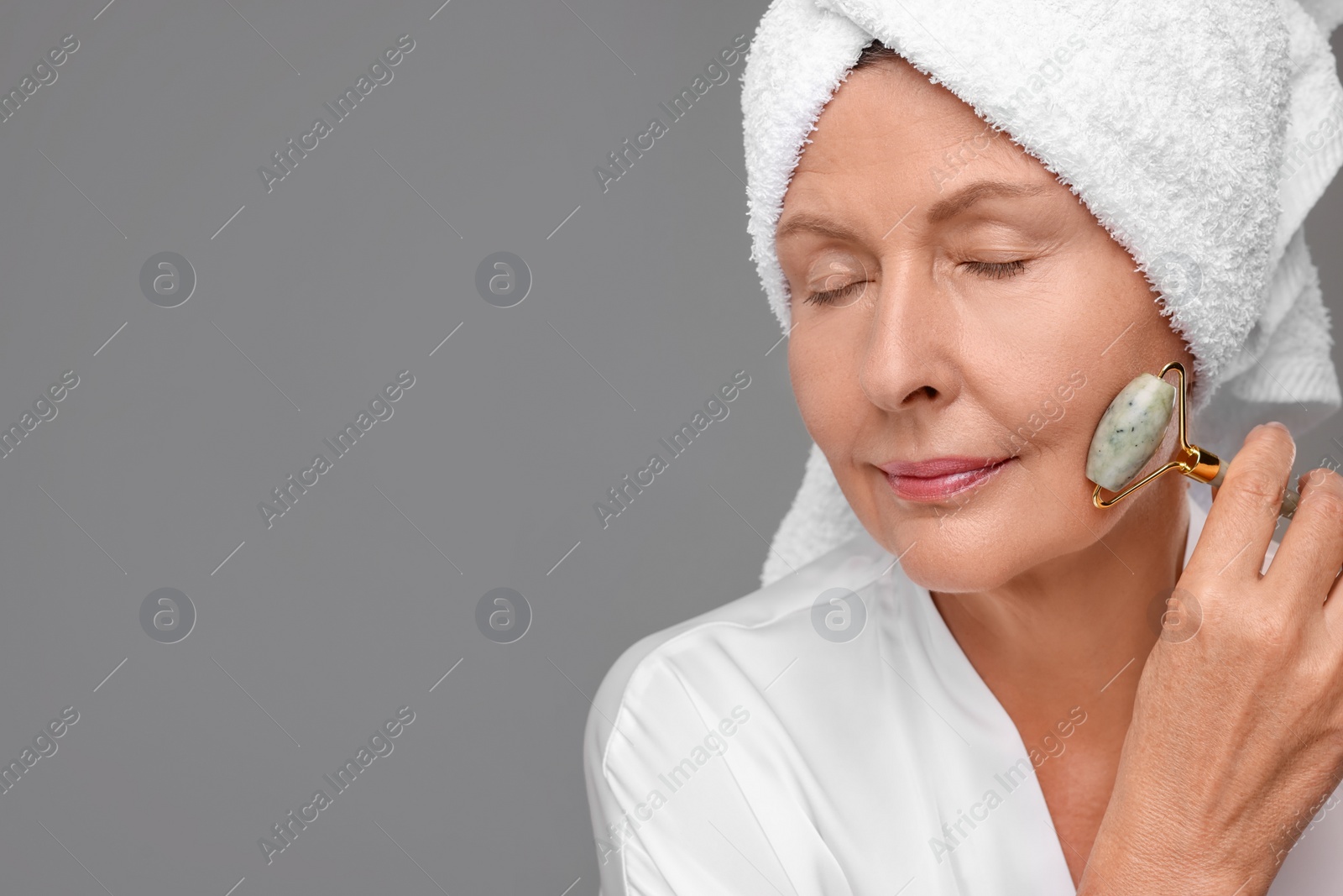Photo of Woman massaging her face with jade roller on grey background, space for text