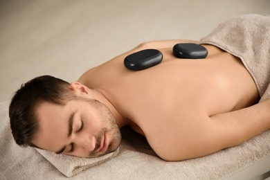 Photo of Handsome man receiving hot stone massage in spa salon