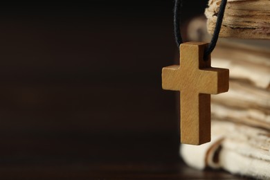 Wooden Christian cross and old books on dark table, closeup. Space for text