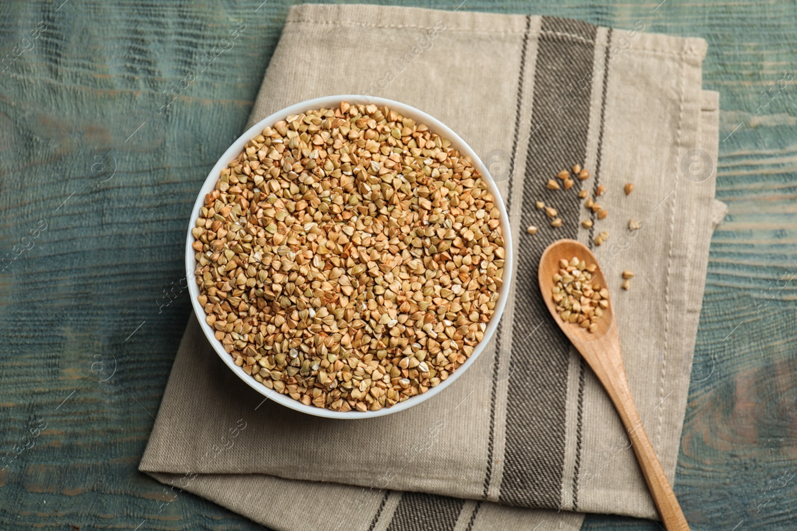 Photo of Uncooked green buckwheat grains on light blue wooden table, flat lay