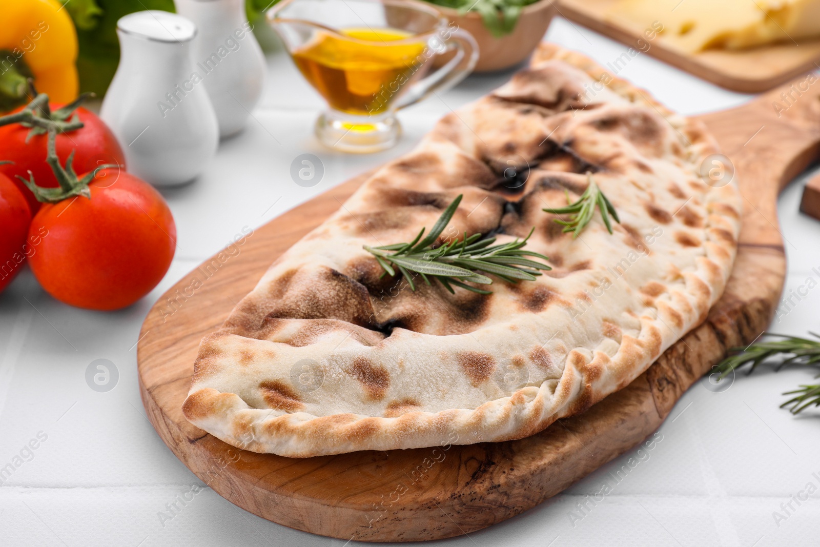 Photo of Tasty pizza calzone with rosemary and different products on white table, closeup