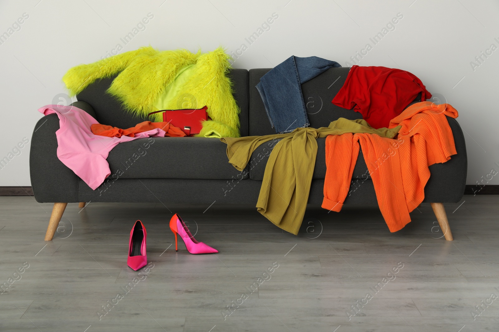 Photo of Messy pile of colorful clothes on sofa and shoes in living room