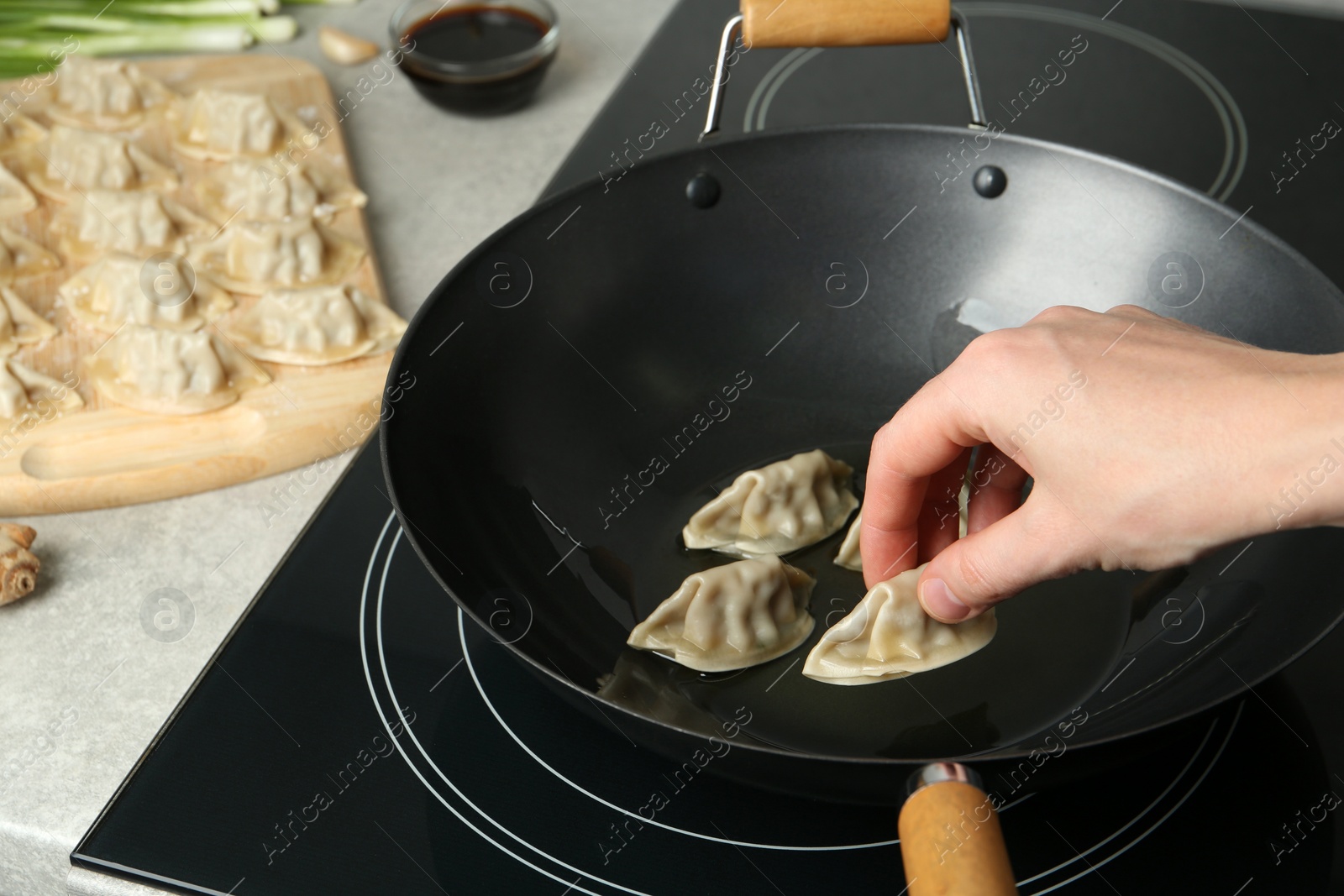 Photo of Woman putting raw gyoza on frying pan with hot oil, closeup