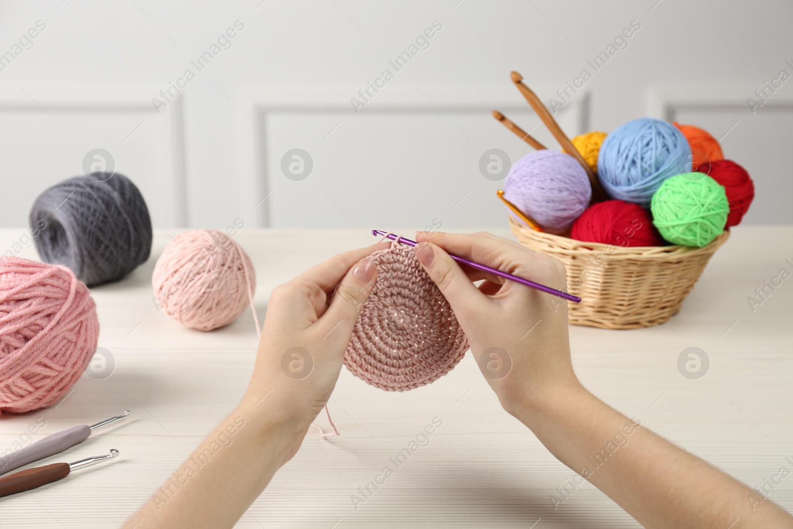 Photo of Woman crocheting with pink thread at white wooden table, closeup