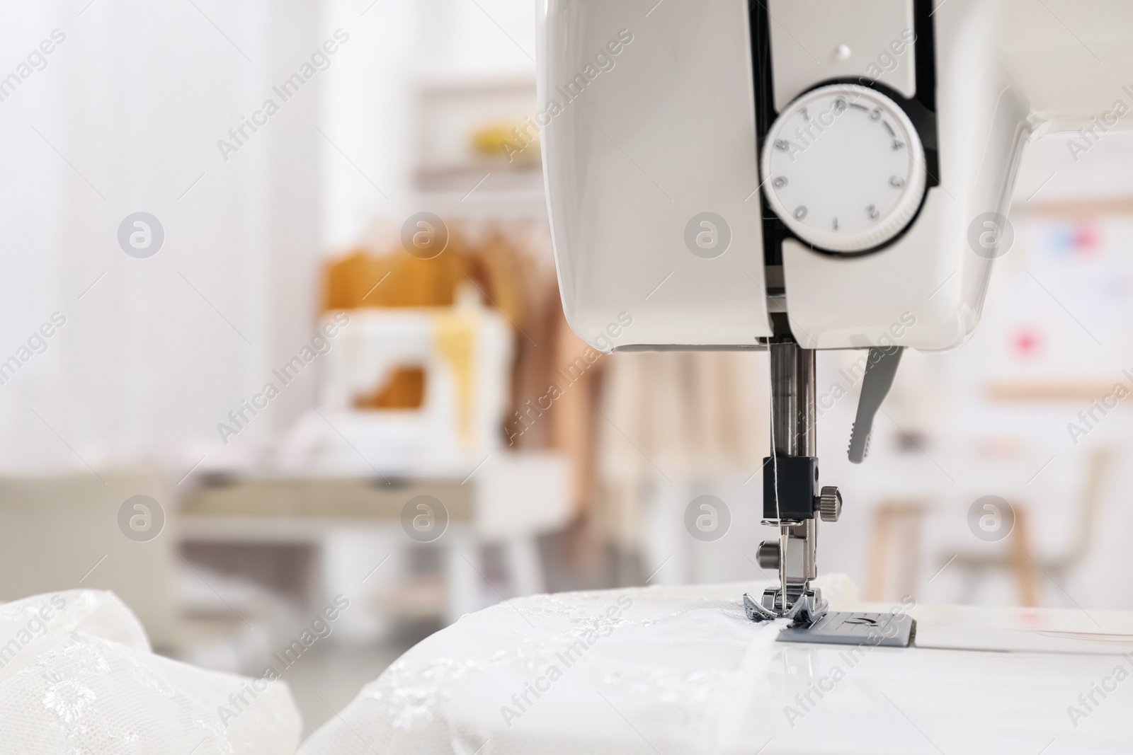 Photo of Modern sewing machine with fabric in dressmaking workshop, closeup
