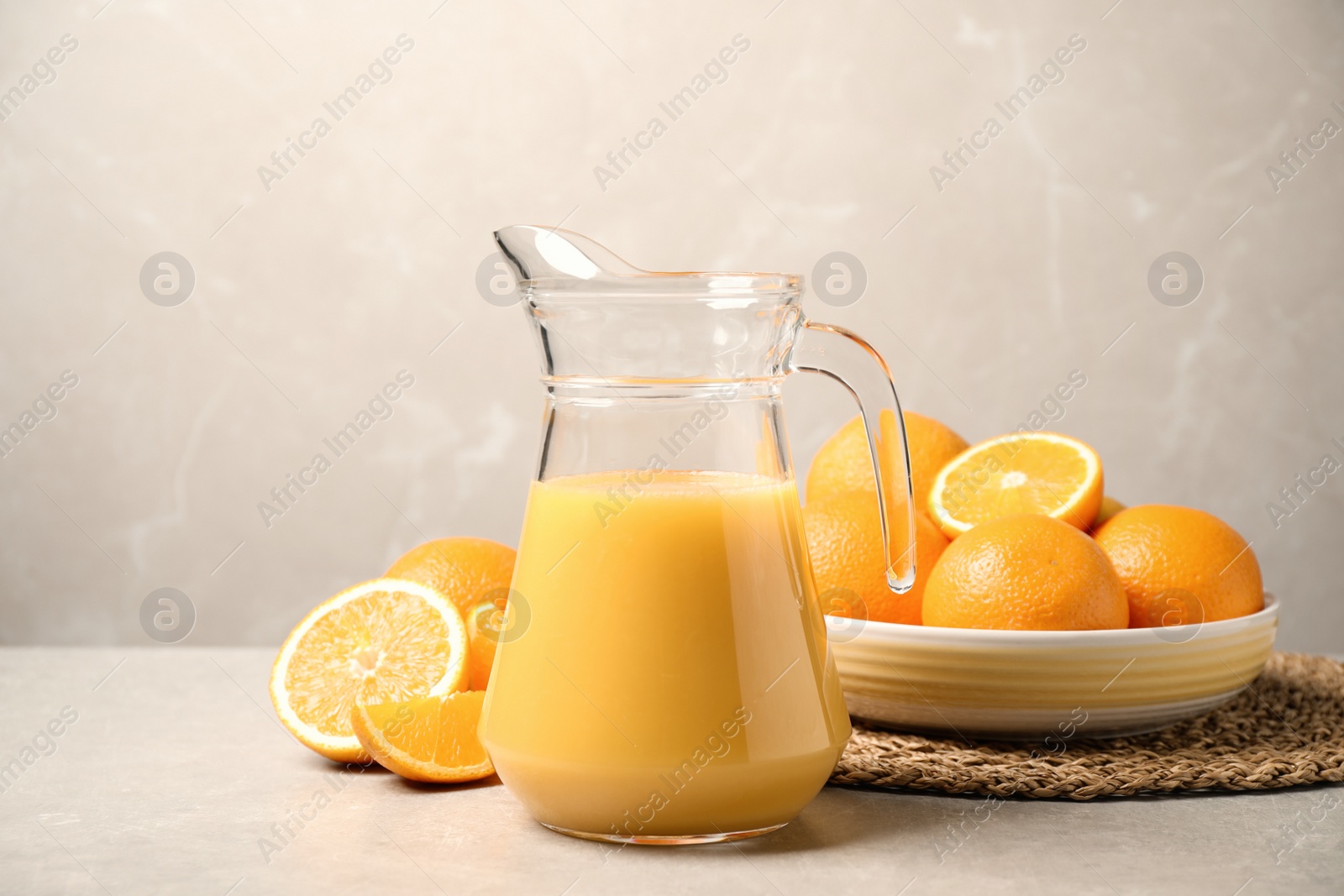 Photo of Jug of orange juice and fresh fruits on light grey table