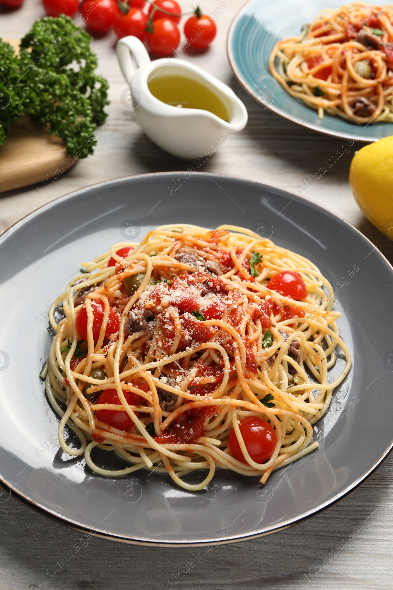 Photo of Delicious pasta with anchovies, tomatoes and parmesan cheese served on white wooden table