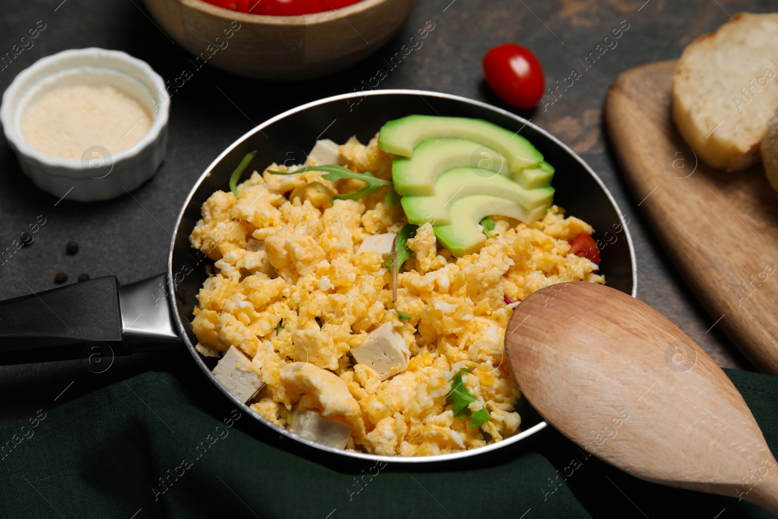 Photo of Frying pan with delicious scrambled eggs, tofu and avocado on black table