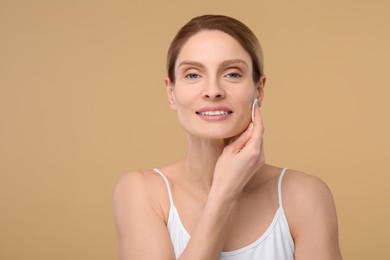Beautiful woman removing makeup with cotton pad on beige background