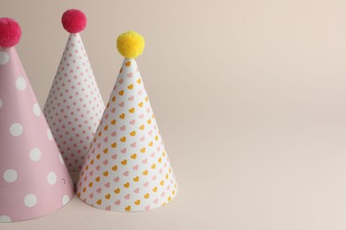 Photo of Beautiful party hats with pompoms on beige background. Space for text