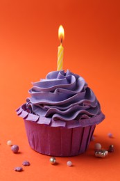 Photo of Delicious birthday cupcake with burning candle and sprinkles on coral background, closeup