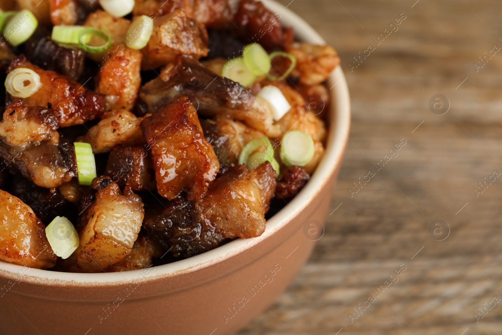 Photo of Tasty fried cracklings in bowl on table, closeup with space for text. Cooked pork lard