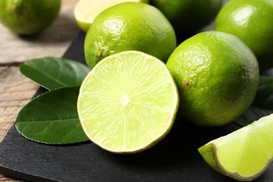 Photo of Fresh limes and green leaves on black board, closeup