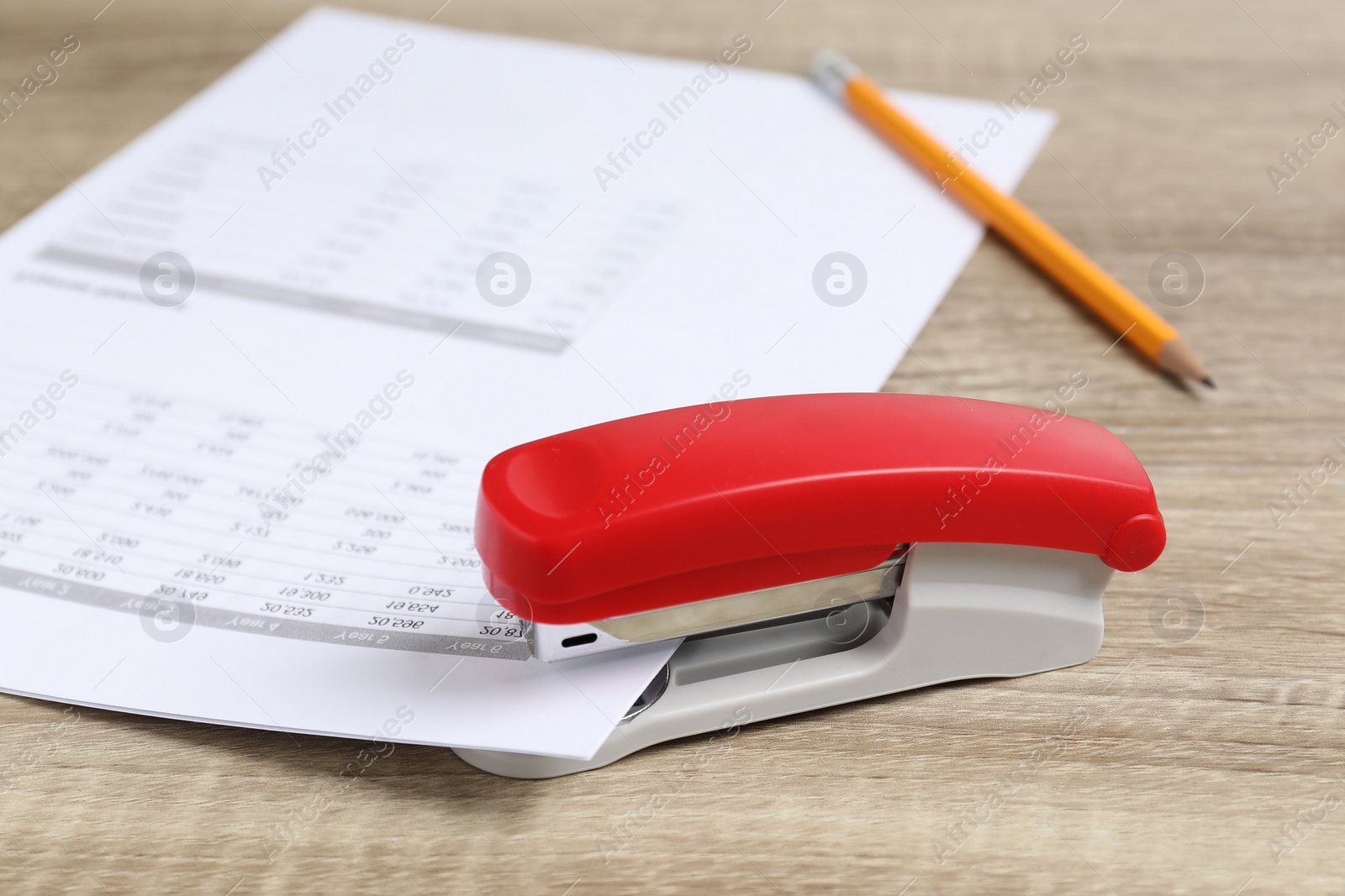 Photo of Bright stapler with documents on wooden table, closeup