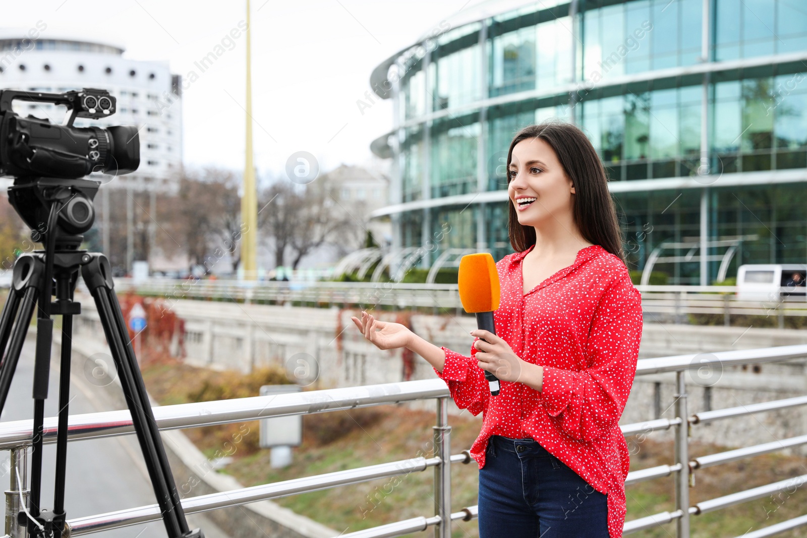 Photo of Young female journalist with microphone working on city street