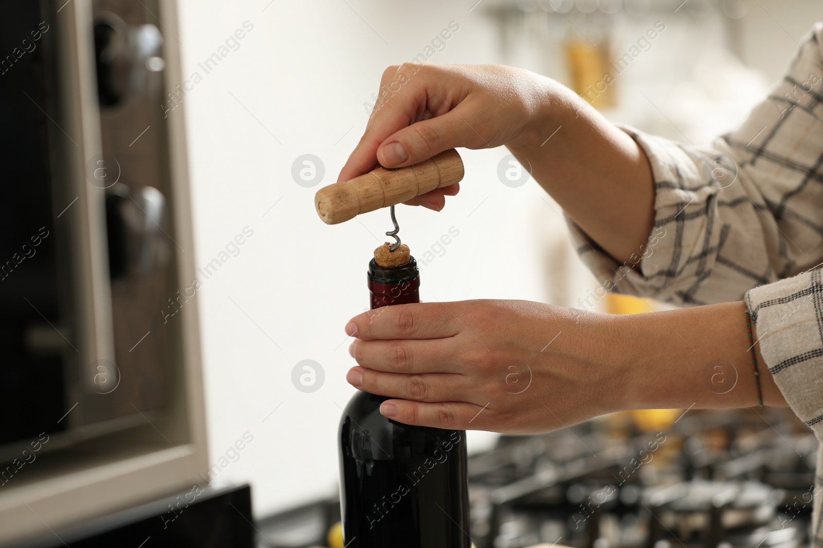 Photo of Woman opening wine bottle with corkscrew indoors, closeup