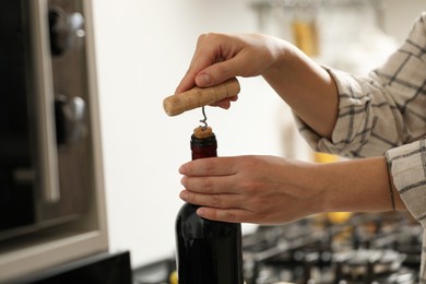 Woman opening wine bottle with corkscrew indoors, closeup