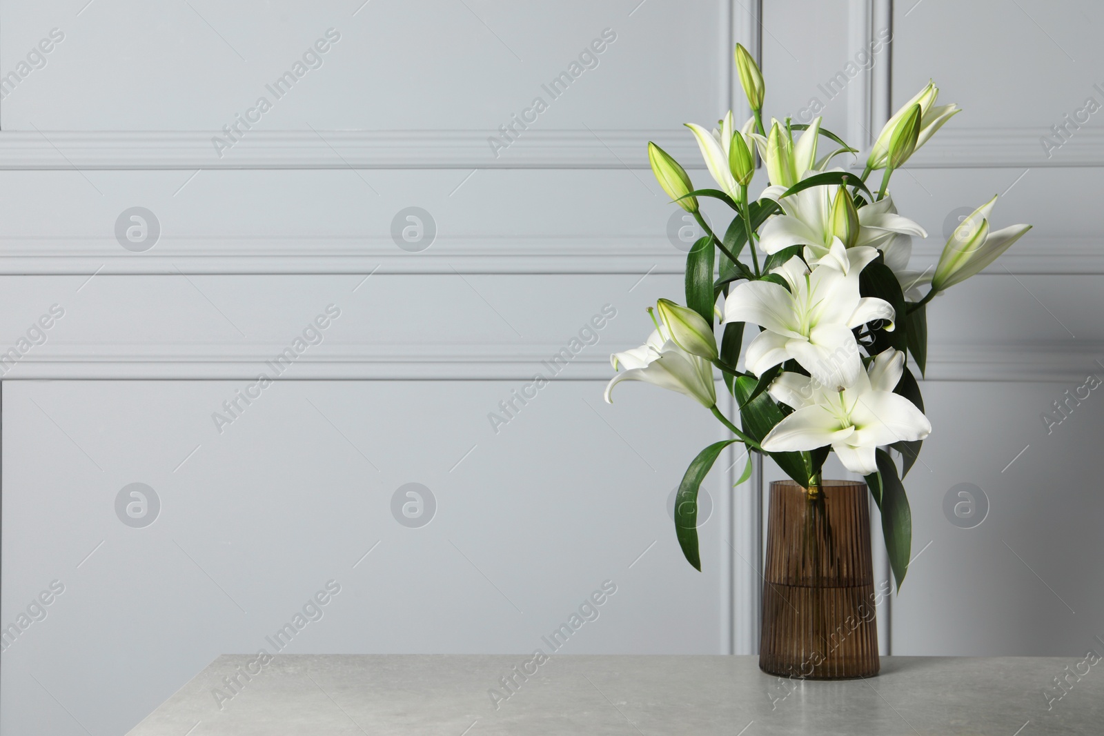 Photo of Beautiful bouquet of lily flowers in glass vase on light grey table, space for text