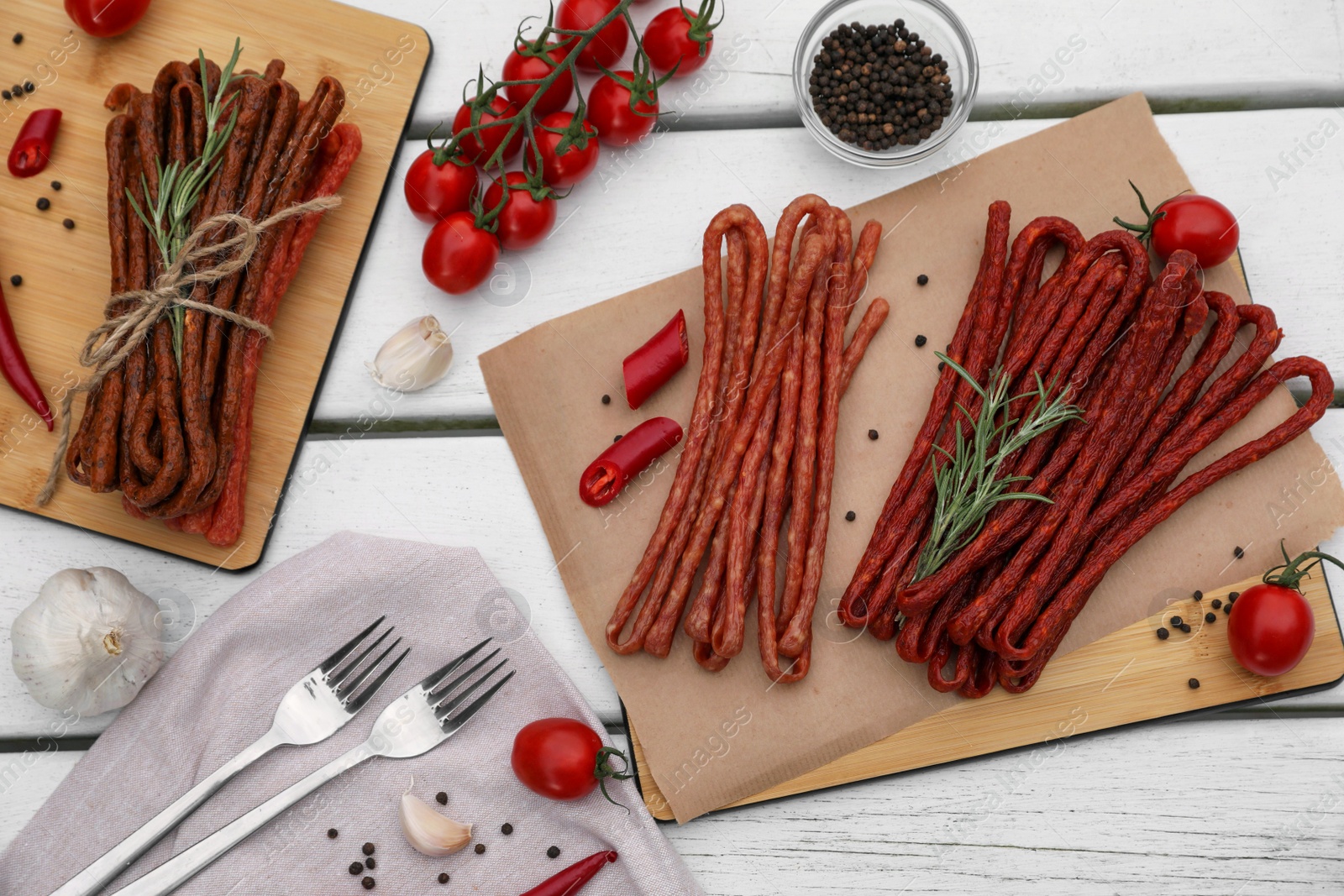 Photo of Delicious kabanosy with rosemary, peppercorn, chilli and tomatoes on white wooden table, flat lay