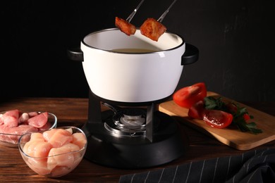 Dipping pieces of fried meat into oil in fondue pot at wooden table