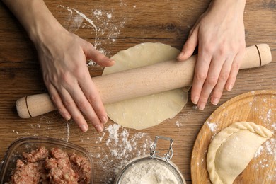 Photo of Woman rolling dough for chebureki on wooden table, top view