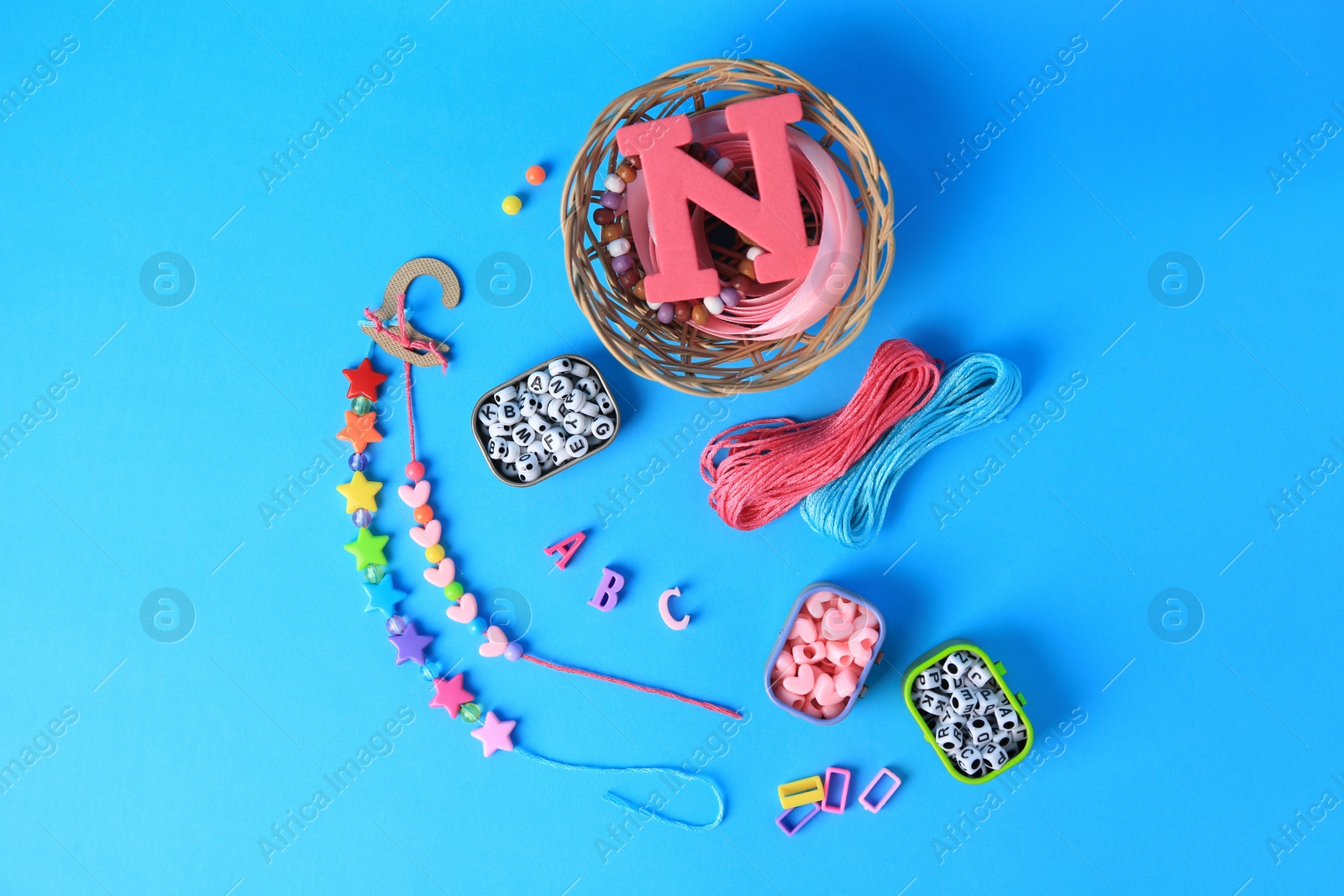 Photo of Handmade jewelry kit for kids. Colorful beads, ribbon and bracelets on light blue background, flat lay