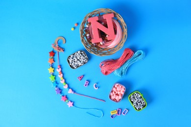 Photo of Handmade jewelry kit for kids. Colorful beads, ribbon and bracelets on light blue background, flat lay