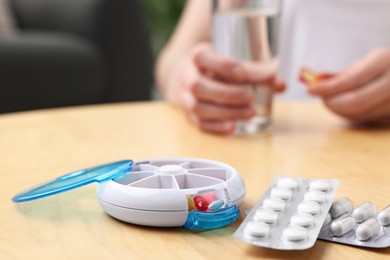 Woman with pills and organizer at light wooden table, selective focus