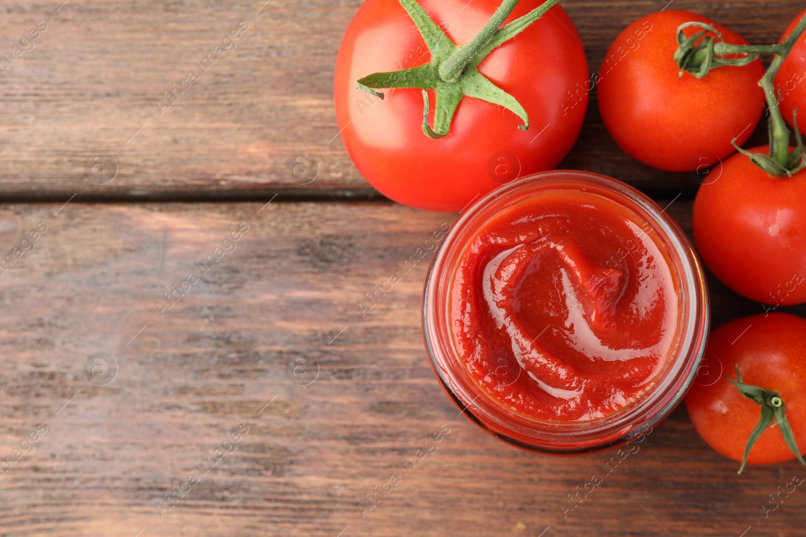 Photo of Jar of tasty ketchup and tomatoes on wooden table, flat lay. Space for text