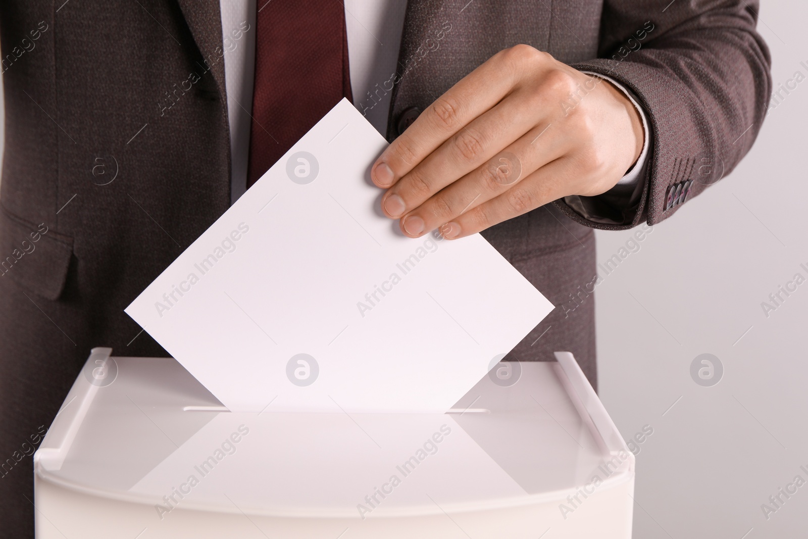 Photo of Man putting his vote into ballot box on light grey background, closeup