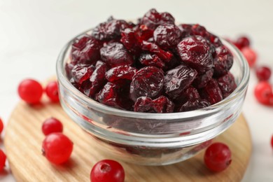 Tasty dried cranberries in bowl and fresh ones on white table, closeup