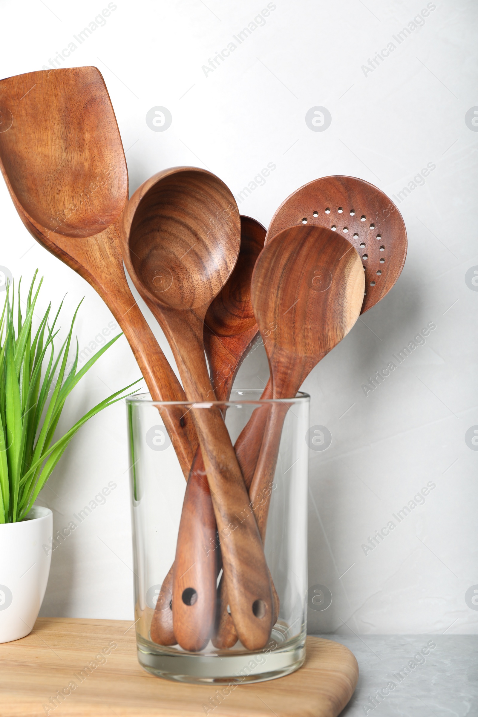 Photo of Set of wooden kitchen utensils in glass holder and houseplant on light grey marble table